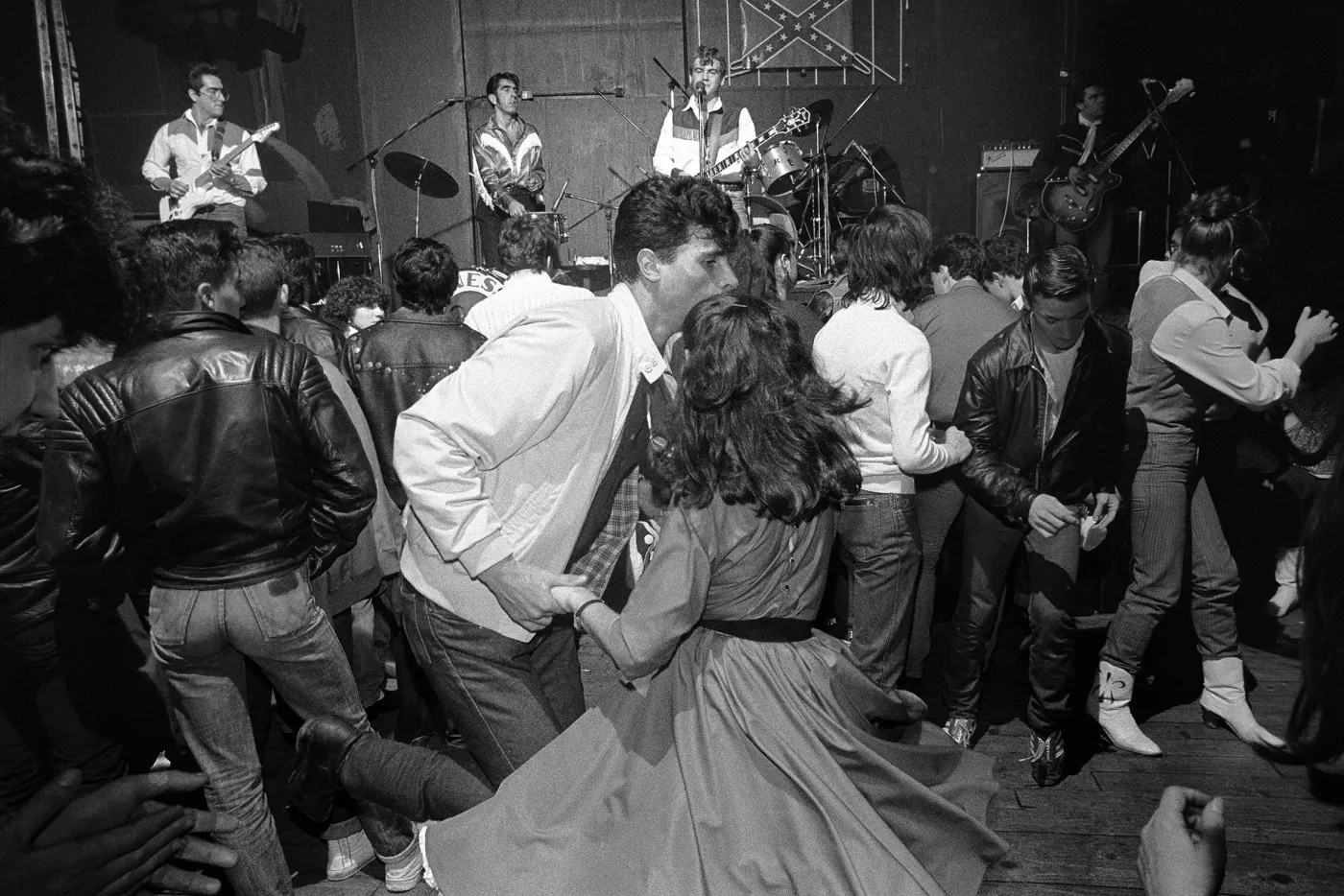 a crowd dancing in couples, a band on stage behind them