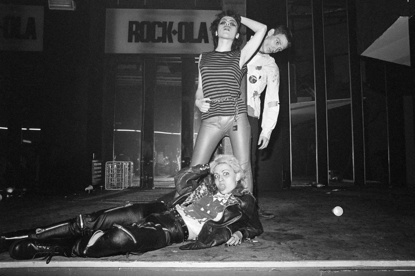 punks posing on the pavement under the rock-ola sign at night